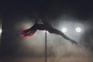 Fototapeta na wymiar Young slim woman pole dancing in dark interior with lights and smoke.
