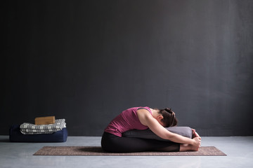 woman practicing yoga, doing Seated forward bend pose, using bolster.