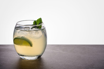 A mojito cocktail in a small oval glass garnished with mint and lime on a stone rock base and back lit background
