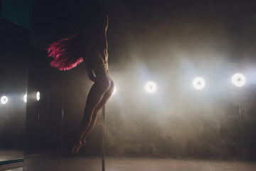 Young slim woman pole dancing in dark interior with lights and smoke.