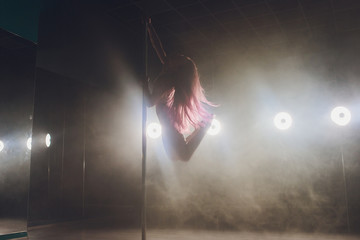 Young slim woman pole dancing in dark interior with lights and smoke.
