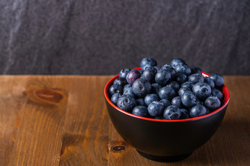 A close up shot of fresh organic blueberries in a red bowl with a wooden base and a rock background