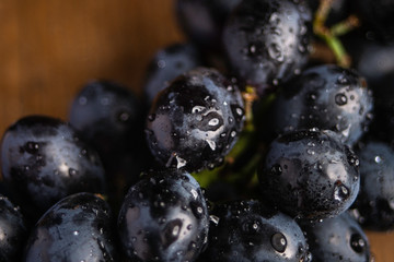 A close up macro photograph of fresh organic vitoria black grapes on the vine with a wooden background