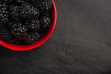 A close up macro overhead photograph of fresh washed organic blackberries in a red bowl with water...