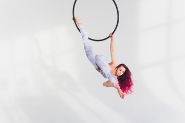 young redhead woman performs acrobatic elements in the air ring on a white background. © Евгений Вершинин