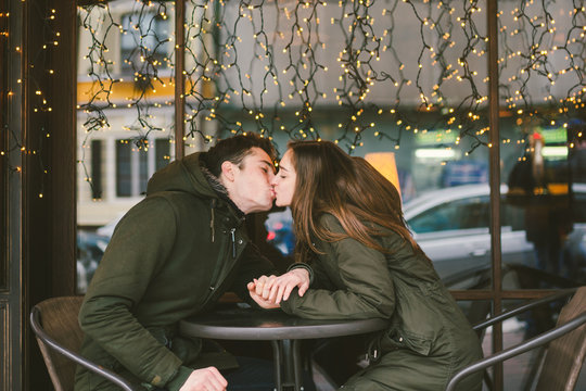 Theme love holiday Valentines Day. pair college students, Caucasian heterosexual lovers in winter, sit table of street cafe against the background window lights. Emotion romance of happiness and love