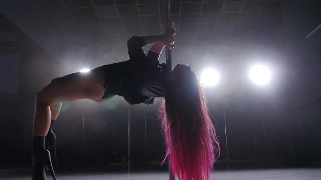 Dance and acrobatics concept. Sexy woman pole dancing in dark interior with lights and smoke
