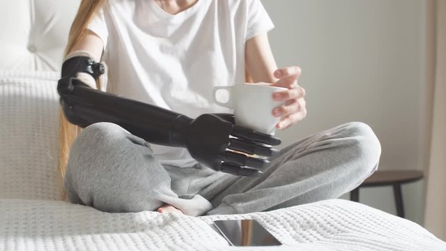 Pleasant girl testing her cyber arm, woman tries to hold a cup with a robotic hand.