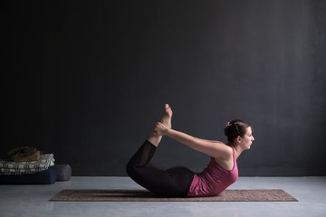 Fototapeta na wymiar Young woman practicing yoga Bow pose, Dhanurasana.