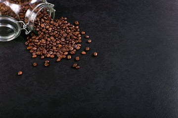 Fragrant coffee beans are scattered from a jar on a rustic tabletop background. Banner copy space.
