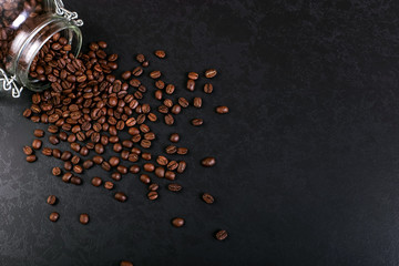 Fragrant coffee beans are scattered from a jar on a rustic tabletop background. Banner copy space.