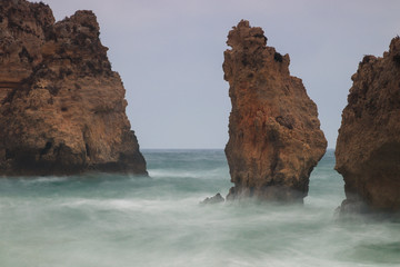 Rocks and pillars in the ocean at Lagos, Algarve, Portugal during high waves and wind. Showing movement of the water during the first storm of the year with long exposure. Beautiful tourist attraction