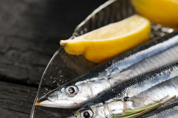 raw saury on a glass dish in the form of fish with rosemary and lemon