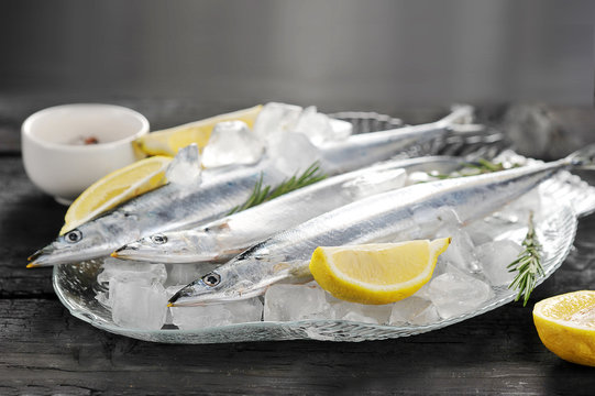 raw saury on a glass dish in the form of fish with rosemary and lemon