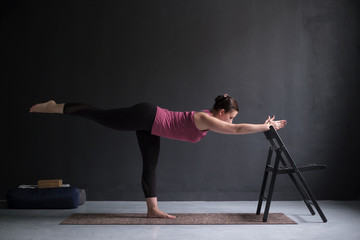 Woman show warrior asana using chair in studio background