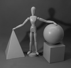 Tabletopfoto mit Gliederpuppe , Pyramide, Würfel und Kugel in Grautönen