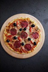 Pizza with salami, mozzarella cheese, cherry tomatoes, black olives and oregano. Home made food. Concept for a tasty and hearty meal. Black stone background. Top view. Copy space