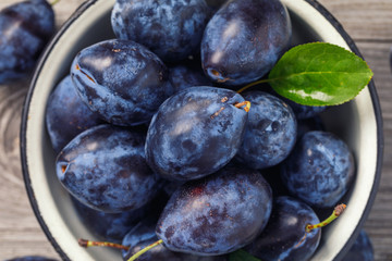 Top view of a bowl full of ripe prune fruit on a wooden table, close-up