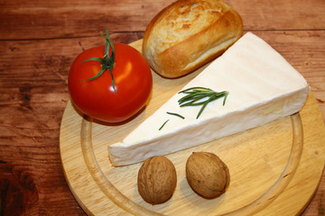 Brie cheese plate with baguette, tomato and nuts on rustic, wooden background.