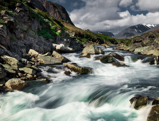 Long exposure of a river with stones in front of mountains while walking Kungsleden (Kings path) hike in northern Sweden during summer. 