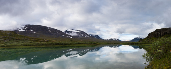 Panorama of Alesjaure lake with mountains behind creating refletioctions just before sunrise. Captured while walking Kungsleden (Kings path) in northern Sweden. Just outside Alesjaure cabin.