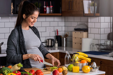 Beautiful smiling young pregnant woman preparing healthy food with lots of fruit and vegetables at home kitchen - Powered by Adobe