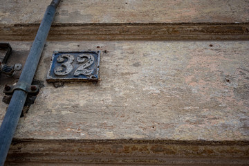 Old weathered cast-iron street plate with number 32, thirty-two, covered with scuffed blue paint in downtown Sofia, Bulgaria in moody cloudy autumn day as seen from city street, low angle view