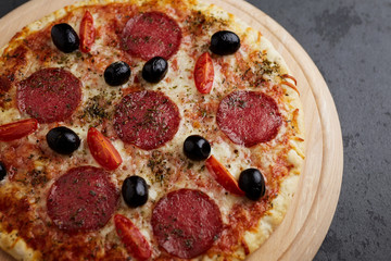 Pizza with salami, mozzarella cheese, cherry tomatoes, black olives and oregano. Home made food. Concept for a tasty and hearty meal. Black stone background. Copy space