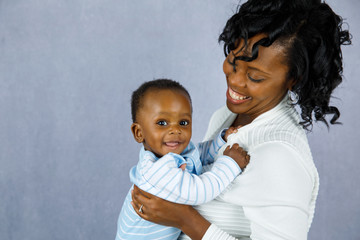 Beautiful African Amercian Woman wHolding Her Baby boy on a Gray Background