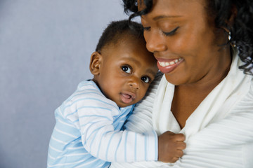 Beautiful African Amercian Woman wHolding Her Baby boy on a Gray Background