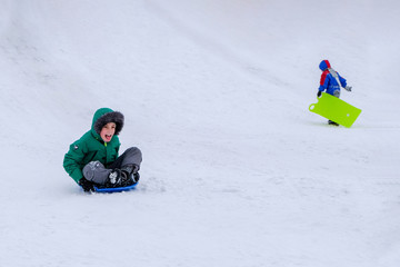 A happy, cheerful, laughing boy in bright clothes in winter is rolling down a slide on a sledge disc over white snow with speed. Place for text.