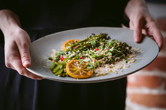 Close up of woman holding a plate of broccolini and barley