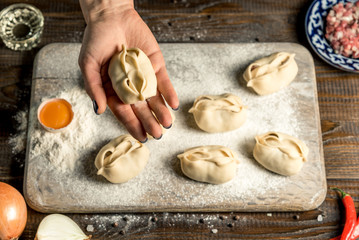Uzbek national food manta, like dumplings, on a wooden board, lie in flour with an egg. Hand holds manta