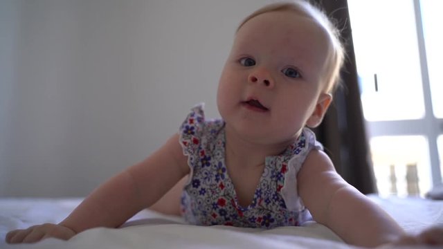 Cute baby face with blue eyes. Close up of little baby. Portrait of infant baby standing in bed and looking around.