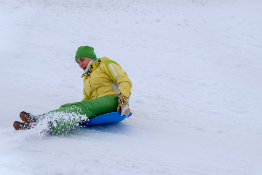 The woman is riding on the sledge or snow disc, laughs and turns over, comes down from the mountain. The concept of joy and a healthy lifestyle.