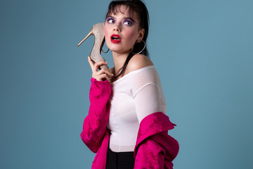 Fashion young woman with colorful makeup using a high heel shoe like a telephone