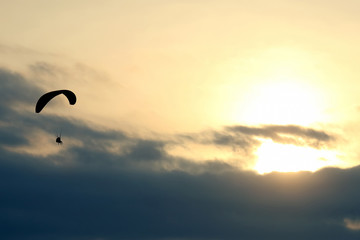 Paraglider flying on a wing in the sky against the setting sun