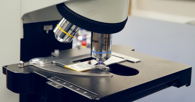 Close up on microscope lenses and a slide with human cancer cells in a science and medical research lab classroom.