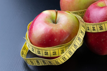 Tasty, ripe apples wrapped in a measuring tape. Fruit on a dark table.