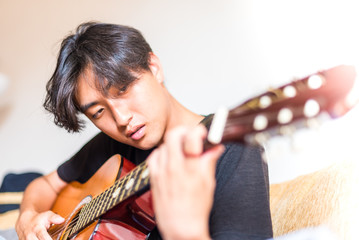 Young asian man playing spanish guitar indoors.