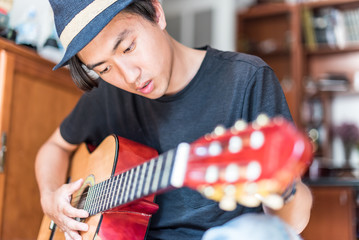 Young asian man playing spanish guitar indoors.