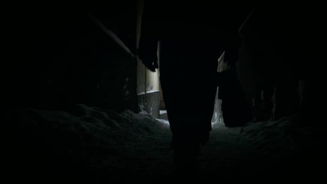 Bottom angle: Man ib black cloak walking through alley