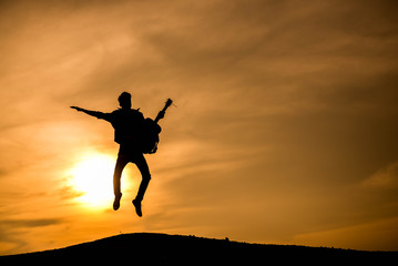 Silhouette Young man jumping with guitar at sunset.