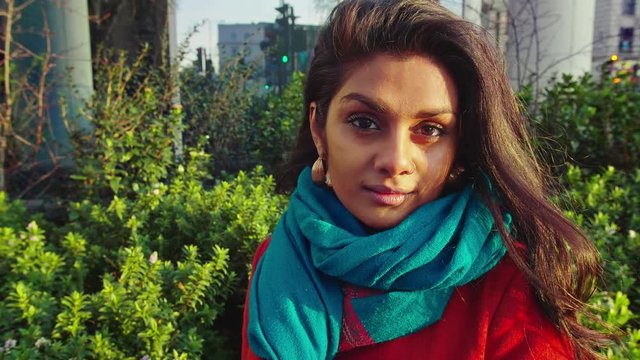 Close up of beautiful young lady sitting in sun in fornt of office building looking into camera before looking up into setting sun slow motion