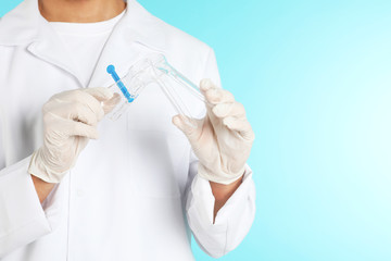 Male doctor holding disposable speculum on color background, closeup with space for text. Medical object