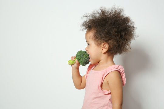 Cute African-American girl eating broccoli on white background. Space for text