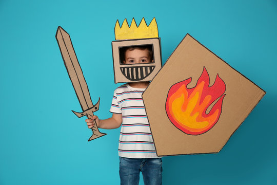 Cute little child in cardboard armor on color background