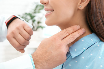 Doctor checking young woman's pulse with fingers in hospital, closeup