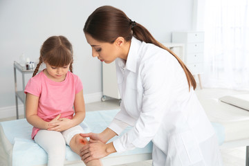 Female doctor examining little girl's injured leg in clinic. First aid