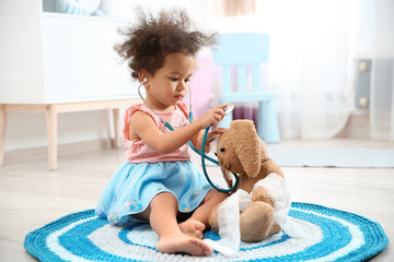 Cute African American child imagining herself as doctor while playing with stethoscope and toy...
